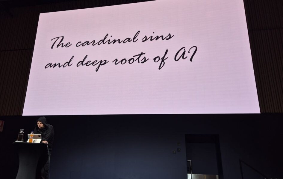 Jouni Heikniemi at the lectern under his closing keynote title slide, The cardinal sins and deep roots of AI, HELish Summit 2026