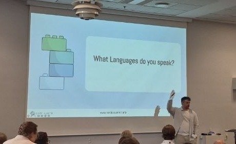 Sebastian Sieber with his hand up asking the room what languages do you speak, LEGO bricks on the slide